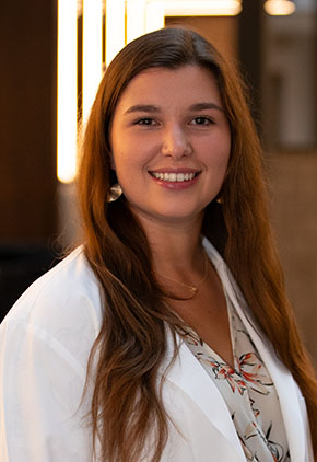 Dr. Emma Eldridge smiles for a headshot in the lobby of BluePearl Pet Hospital. She is wearing a tan floral blouse and her whitecoat.