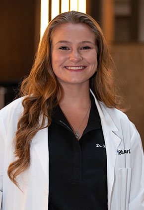 Dr. Karis Littlepage smiles for a headshot in the lobby of BluePearl Pet Hospital. She is wearing black scrubs and her whitecaot.