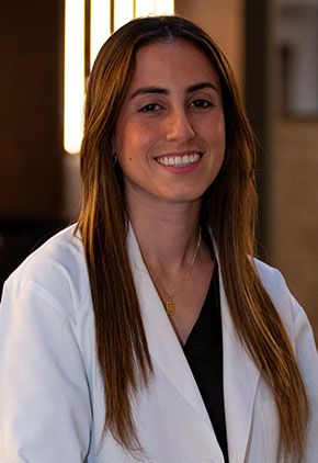 Dr. Luciris Janet Perez Caraballo smiles for a headshot in the lobby of BluePearl Pet Hospital. She is wearing black scrubs and her whitecoat.
