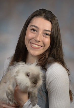 Dr. Amanda Lazar smiles for a professional photo while she holds her grey rabbit in her hands.