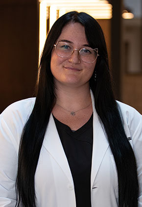 Dr. Madison Hammond smiles for a headshot in the lobby of BluePearl Pet Hospital. She is wearing black scrubs and her whitecoat.