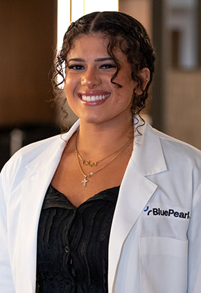 Dr. Diana Ibrahim smiles for a headshot in the lobby of BluePearl Pet Hospital. She is wearing black scrubs and her whitecoat.