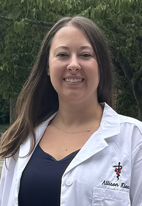 Dr. Allison Klenk smiles outside in her university whitecoat.