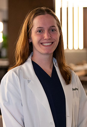 Dr. Nicole Remes smiles for a headshot in the lobby of BluePearl Pet Hospital. She is wearing black scrubs and her whitecoat.