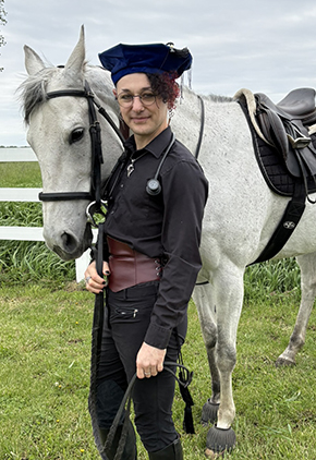 Dr. Dominic D'Andrea smiles outside while holding onto their horse's lead.