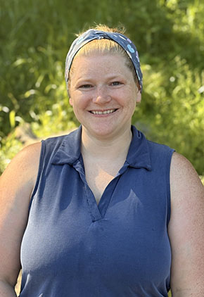 Dr. Shannon Ankney smiles outside in front of lush greenery. She is wearing a navy top and has a navy headband in her hair.
