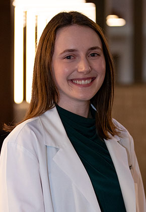 Dr. Mariles Carter smiles for a headshot in the lobby of BluePearl Pet Hospital. She is wearing a black blouse and her whitecoat.