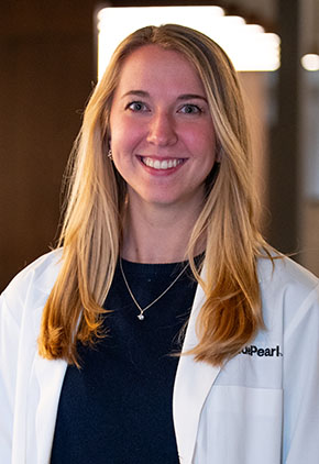 Dr. Cara Hackley smiles for a headshot in the lobby of BluePearl Pet Hospital. She is wearing a black top and her whitecoat.