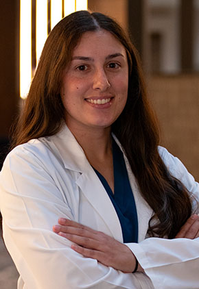 Dr. Annika Miller smiles for a headshot in the lobby of BluePearl Pet Hospital. She is wearing black scrubs and her whitecoat.