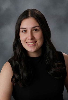 Dr. Annika Miller smiles for a studio headshot in front of a grey backdrop. She is wearing a black sleeveless top.