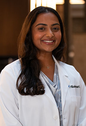 Dr. Sahana Prabhu smiles for a headshot in the lobby of BluePearl Pet Hospital. She is wearing a silver blouse and her whitecoat.