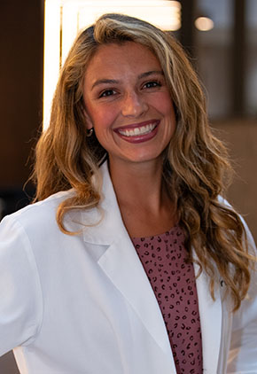 Dr. Savannah Smith smiles for a headshot in the lobby of BluePearl Pet Hospital. She is wearing a brown blouse and her whitecoat.