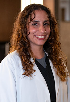 Dr. Jessica Karkar smiles for a headshot in the lobby of BluePearl Pet Hospital. She is wearing black scrubs and her whitecoat.