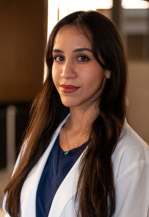 Dr. Beatriz Gutiérrez has a soft smile while posing for a headshot in the lobby of BluePearl Pet Hospital. She is wearing a black blouse and her whitecoat.