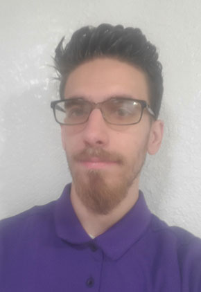 Dr. Stephen Zachary Trombetta softly smiles for a headshot in front of a white wall. He is wearing a purple polo.