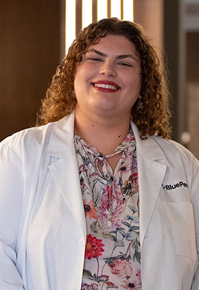 Dr. Hailey Hunter smiles for a headshot in the lobby of BluePearl Pet Hospital. She is wearing a white shirt featuring red and pink flowers as well as her whitecoat.