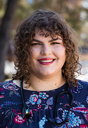 Dr. Hailey Hunter smiles outside for a professional headshot. She is wearing a blue and pink paisley blouse and has a stethoscope around her neck.