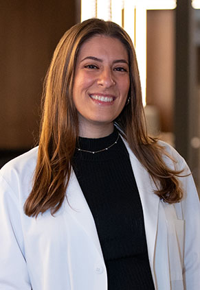 Dr. Cecile Koceyan smiles for a headshot in the lobby of BluePearl Pet Hospital. She is wearing a black blouse and her whitecoat.