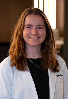 Dr. Sarah Teter smiles for a headshot in the lobby of BluePearl Pet Hospital. She is wearing a black top and her BluePearl whitecoat.