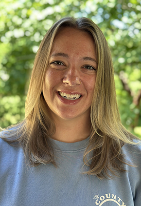 Dr. Hannah May smiles outside for a headshot. She is wearing a heather blue top.