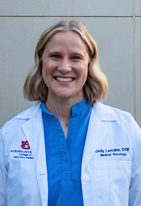 Dr. Emily Lemoine smiles outside in front of a building wall. She is wearing a blue blouse and her Auburn University whitecoat.