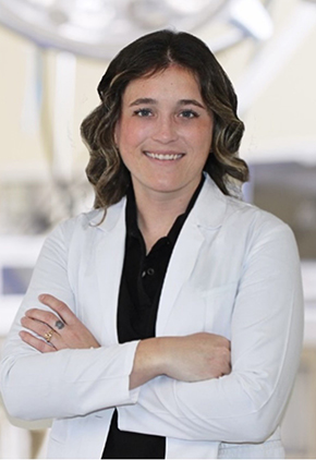 Dr. Shelby Scanlin smiles for a headshot. She is wearing a black blouse, her whitecoat and has her arms crossed across her chest.