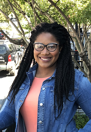 Dr. Sheridan Dillon-Robinson smiles outside on a sunny day. She is wearing a peach blouse and chambray shirt.