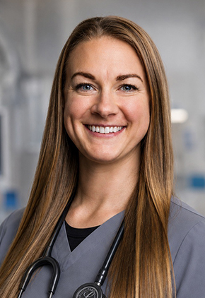 Dr. Christin Reminga smiles for a headshot in the hospital. She is wearing grey scrubs and has a stethoscope around her neck.