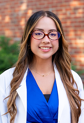 Dr. Melanie Figueroa-Cordeo smiles outside for a professional headshot. She is a royal blue blouse and her BluePearl whitecoat.