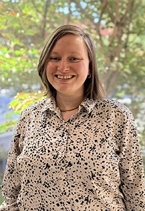 Dr. Enjolie Levengood smiles outside in front of a tree. She is wearing a white blouse that features black abstract spots.