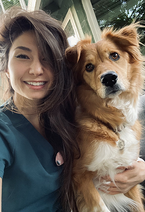 Dr. Christine Boles smiles for a selfie with her Australian shepherd. She is wearing evergreen scrubs.