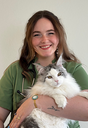 Dr. Grace Linden-Santangeli smiles for a headshot while holding her white Maine coon in her arms. She is in green scrubs and has a stethoscope around her neck.