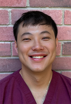 Dr. Zong Peng smiles outside in front of a brick building. He is wearing maroon scrubs.