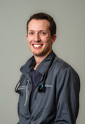Dr. Garrett Ballou smiles for a professional headshot. He is wearing a grey athletic jacket and has a stethoscope around his neck.
